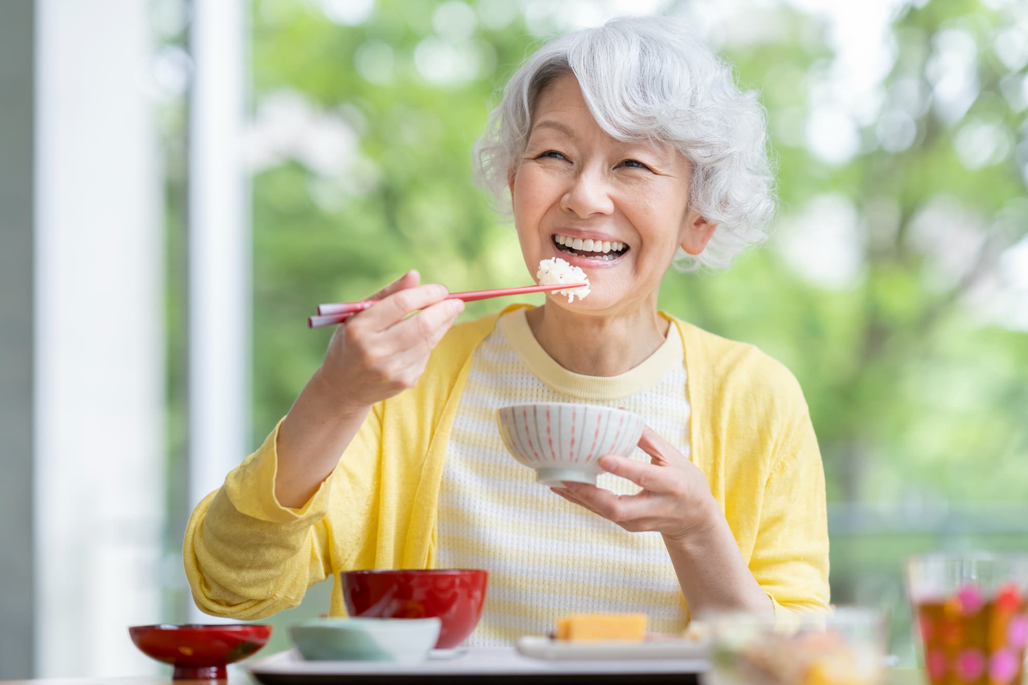 適切なケアで健康な歯を維持しているシニア女性が笑顔で食事をしているイメージ